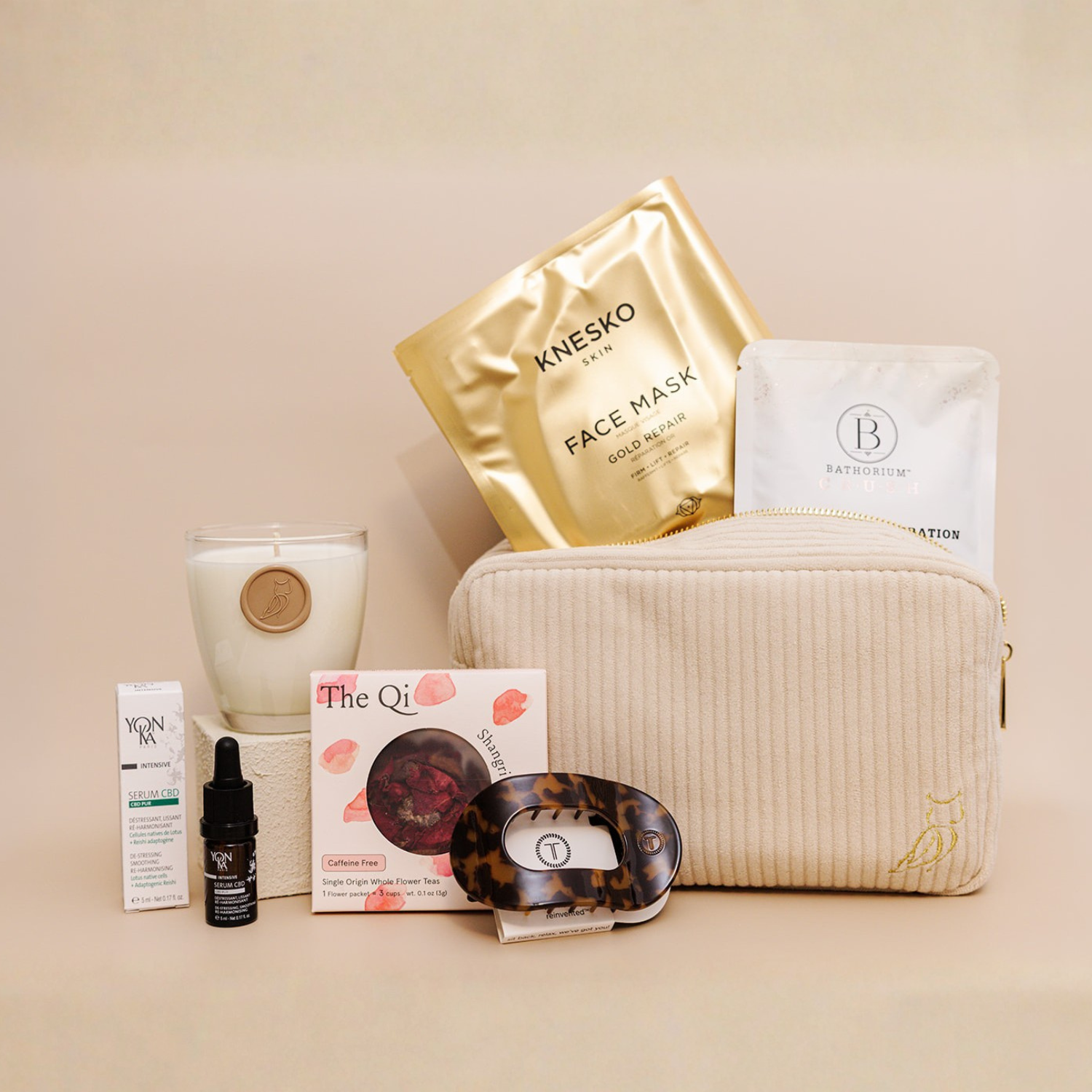 Luxe Bath Ritual Kit | Live Love Spa featuring a soft beige toiletry bag with gold zipper, skincare essentials including a gold face mask, white sachet, scented candle, facial serum, tea, and a tortoiseshell facial massage tool.
