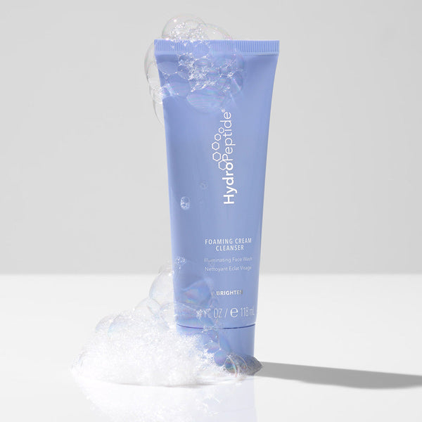 Tube of Foaming Cream Cleanser | HydroPeptide in soft lavender color surrounded by fresh white foam on a clean, light surface, highlighting skincare and body care wellness.