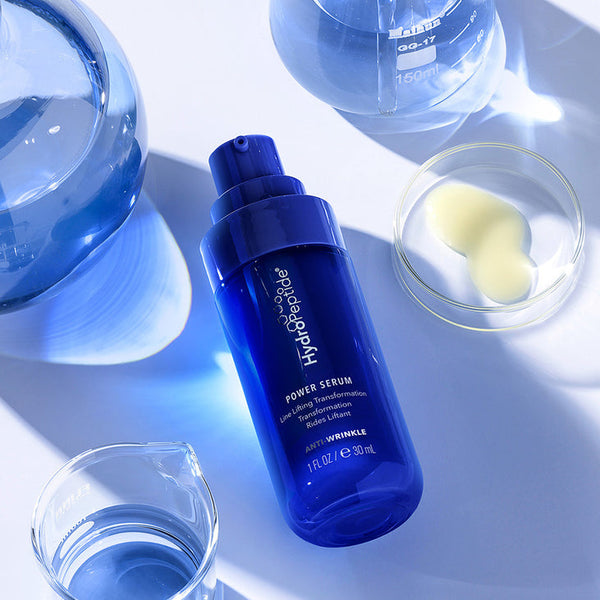 Blue bottle of Power Serum | HydroPeptide placed among clear laboratory glassware with liquid droplets, highlighting skincare and anti-wrinkle treatment in a wellness setting.