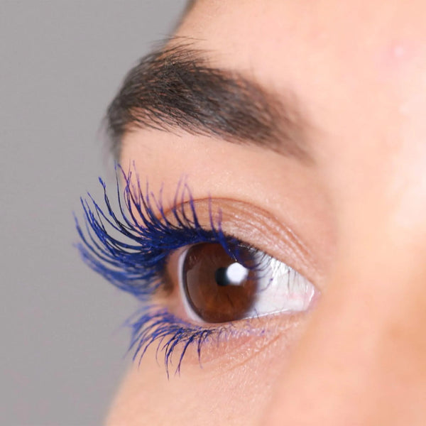 Close-up of a brown eye with long, curled lashes coated in vibrant blue mascara, highlighting the effect of the Deluxe Heated Eyelash Curler | Chella for enhanced lash curl and volume.