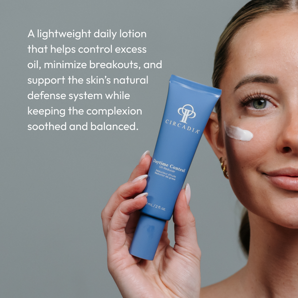 A woman holding a blue tube of Daytime Control Oil Reducer Circadia skincare lotion with a small amount applied on her cheek, promoting a lightweight daily lotion that controls excess oil and soothes the complexion.