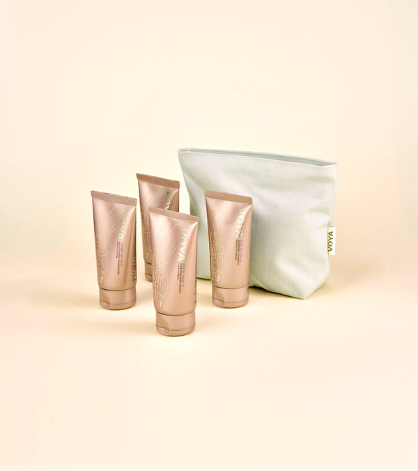 Four rose gold tubes of skincare products arranged next to a white zippered travel pouch labeled with a small VOYA tag, representing the Organic Voyager Travel Set | VOYA.