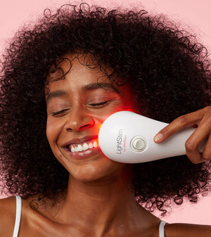 Woman using LightStim For Wrinkles | LightStim device on her cheek, demonstrating skincare and wellness with a gentle red light therapy treatment.