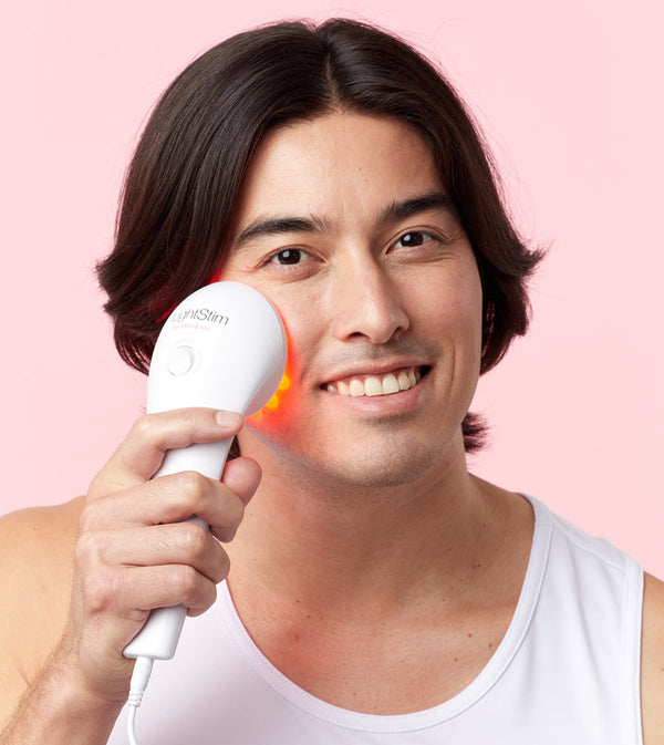 Man using LightStim For Wrinkles | LightStim device on his cheek with a glowing red light, demonstrating skincare and anti-aging treatment at home.