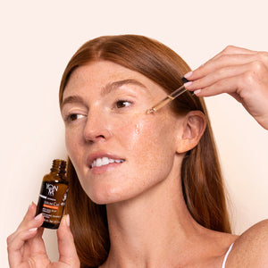 Woman with red hair applying Serum C20 | Yon-Ka Paris to her cheek using a dropper, showcasing skincare application for a glowing complexion.
