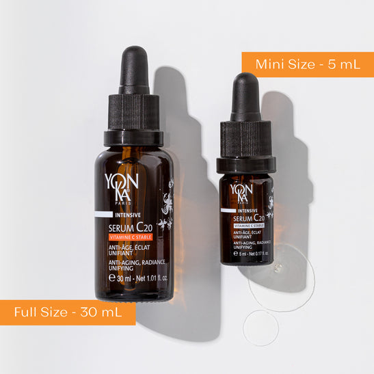 Two amber glass dropper bottles of Serum C20 | Yon-Ka Paris in 30 mL full size and 5 mL mini size with some serum drops next to them on a white background, highlighting anti-aging skincare.