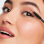 Close-up of a woman applying Lash Fixation Length & Definition Tubing Mascara | Jane Iredale to her upper eyelashes, highlighting long, defined lashes and radiant skin.