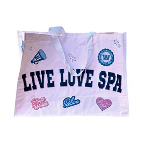 Live Love Spa Collegiate Cuties Event Bag | Live Love Spa features a light pink tote with white handles and collegiate-style navy blue text accented by wellness and self-care themed patches.