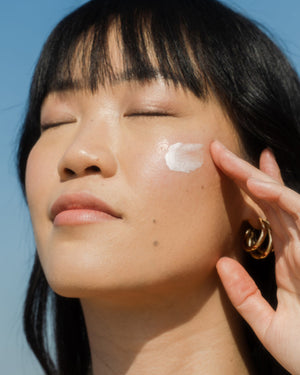Close-up of a woman with eyes closed applying sunscreen on her cheek, demonstrating gentle skincare use with the Suncare Travel Essentials Set | COOLA.