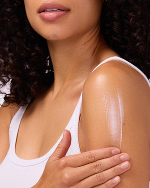 Close-up of a woman applying moisturizing sunscreen lotion on her shoulder, showcasing skin care with the Suncare Travel Essentials Set | COOLA for smooth and protected skin.