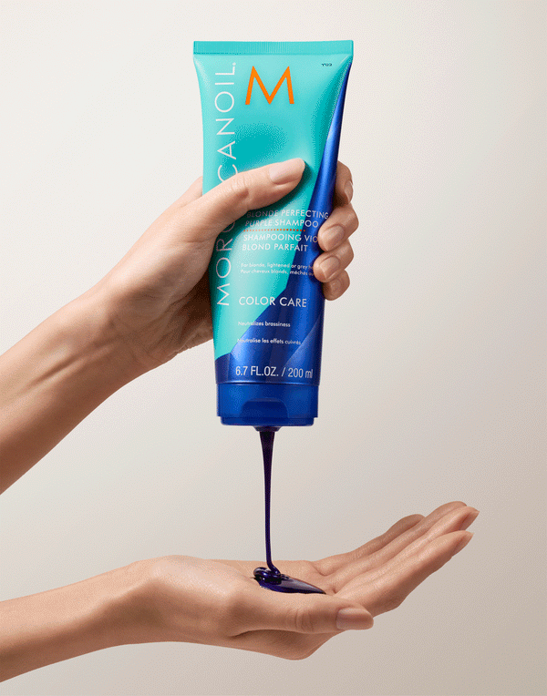 Hand holding a tube dispensing a rich purple shampoo onto the palm, featuring Blonde Perfecting Purple Shampoo | Moroccanoil for color care and toning blonde hair.