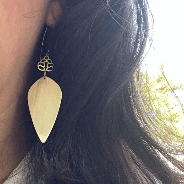 Close-up of a person wearing Brass Droplet Earrings | Purpose Jewelry, featuring a teardrop-shaped brass pendant with intricate detailing at the hook against dark hair.