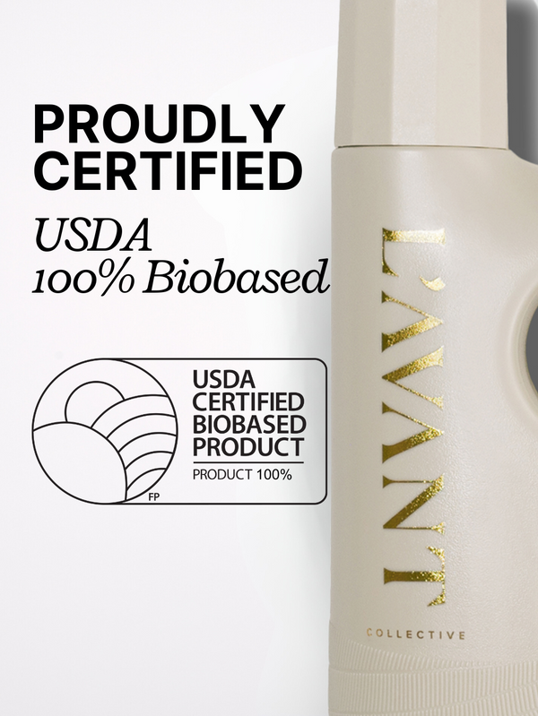 Partial view of a beige bottle with gold lettering showing the text "L'AVANT Collective" alongside a USDA Certified Biobased Product label and the words "Proudly Certified USDA 100% Biobased" promoting High Performing Laundry Detergent - Fresh Linen | L'AVANT Collective.