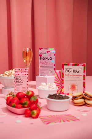 Big Hug - 5 Pack | Popmask self-heating patches displayed on a pink table surrounded by strawberries, popcorn, marshmallows, chocolate, and a glass of beverage, promoting wellness and comfort.