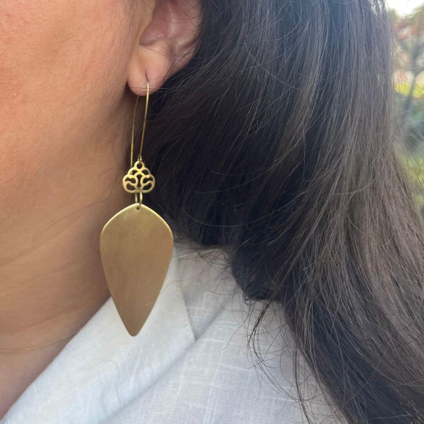 Close-up of a person wearing Brass Droplet Earrings | Purpose Jewelry, featuring a smooth, elongated brass droplet pendant with intricate detailing at the hook.