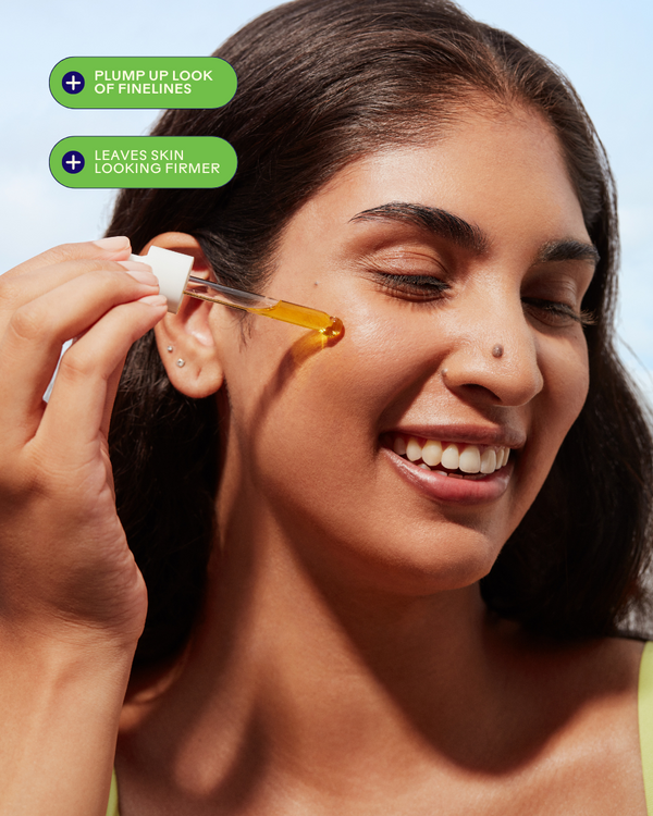 Smiling woman applying Boost 49% Rosehip Oil Serum | Three Ships to her cheek with a dropper, promoting skincare benefits like plumping fine lines and firmer-looking skin.