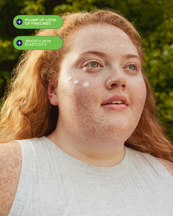 Close-up of a person with fair skin and freckles wearing a sleeveless top, applying SkinHero™ Calendula + 2% Bakuchiol Bio-Retinol Serum | Three Ships on their cheek, highlighting benefits like plumping fine lines and boosting skin elasticity.