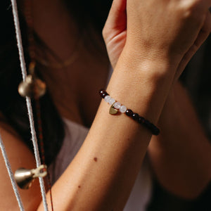 Close-up of a wrist wearing a Gemstone Heart Bracelet | Purpose Jewelry featuring dark and light beads with a small heart-shaped charm, styled for wellness and elegance.