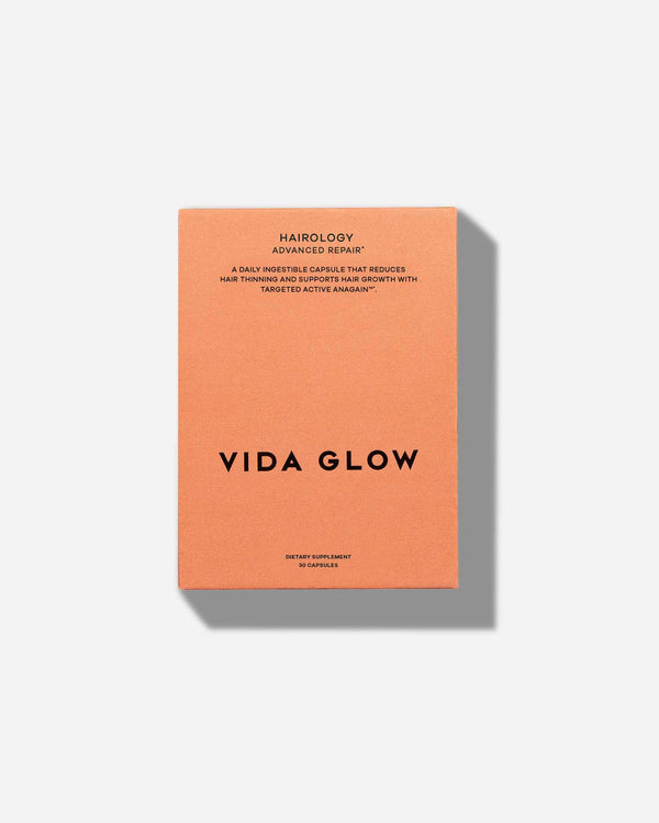 Orange box packaging for Hairology Capsules | VIDA GLOW dietary supplement with text describing it as a daily capsule to reduce hair thinning and support hair growth.