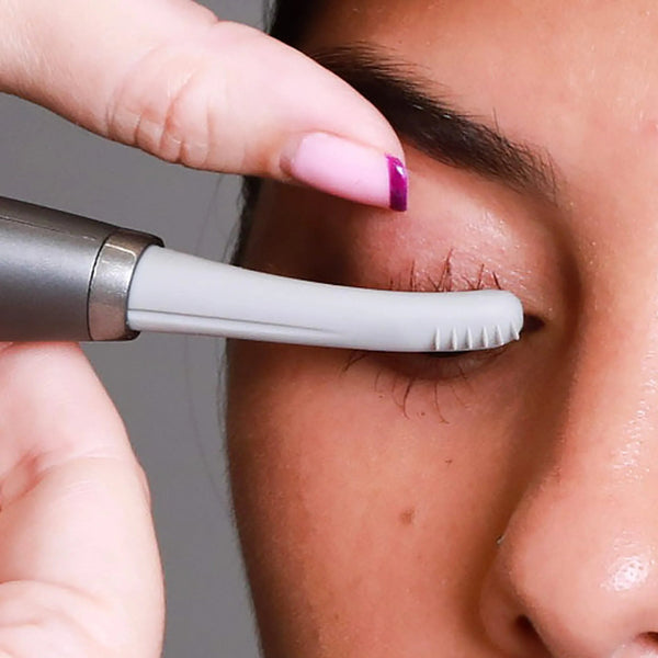 Close-up of a person using the Deluxe Heated Eyelash Curler | Chella to gently curl their eyelashes, showcasing a sleek gray device applied near the upper lashes.
