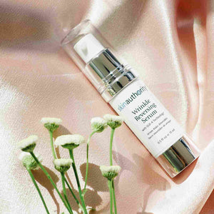 Complete Serum | Skin Authority bottle with a pump dispenser placed on a soft peach satin fabric next to small white flowers, highlighting skincare and wellness themes.