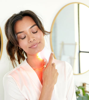 Woman using LightStim For Wrinkles | LightStim device emitting red light on her neck in a bright room with a mirror in the background for skincare and wellness.