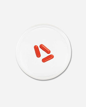 Three red capsules placed inside a clear circular dish on a white background, representing Hairology Capsules | VIDA GLOW wellness supplements.