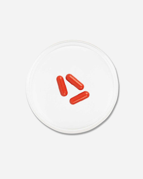 Three red capsules placed inside a clear circular dish on a white background, representing Hairology Capsules | VIDA GLOW wellness supplements.