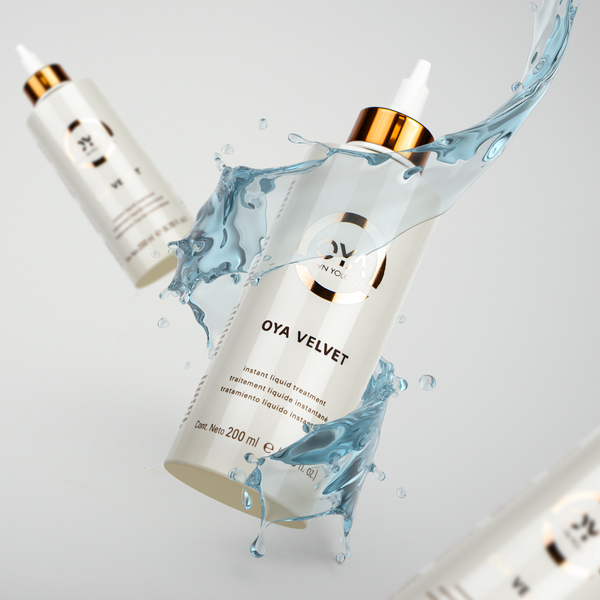 White bottle of Velvet Instant Liquid Treatment | OYA with gold accents surrounded by a splash of clear blue liquid, highlighting its skincare and hydration benefits.