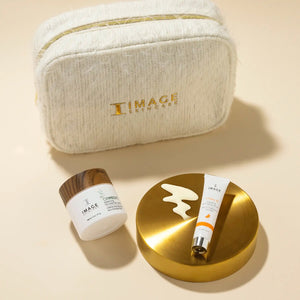 Soft textured cream-colored cosmetic bag with gold zipper and IMAGE Skincare logo, alongside two skincare products displayed on a golden dish, part of Dazzling Duo | IMAGE Skincare.