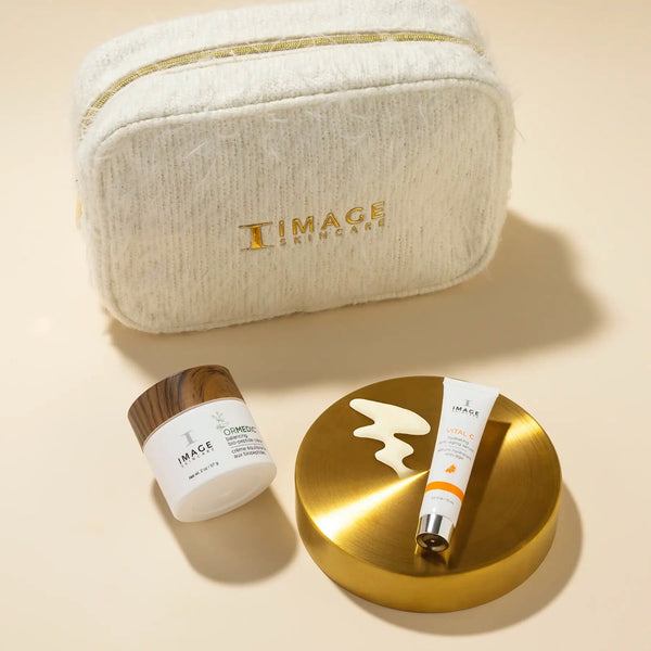 Soft textured cream-colored cosmetic bag with gold zipper and IMAGE Skincare logo, alongside two skincare products displayed on a golden dish, part of Dazzling Duo | IMAGE Skincare.