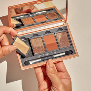 Hands holding the Manifest Bronze Eyeshadow Palette | Chella showcasing three bronze shades with one shimmer shade, a small removable pan, and a dual-ended applicator inside a rose gold compact with a mirror.
