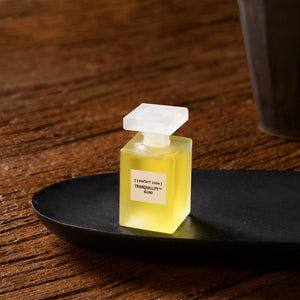 A small frosted glass bottle of oil labeled "Tranquillity Blend" placed on a black dish on a wooden surface, part of The City Serenity Kit | [ comfort zone ] skincare collection.