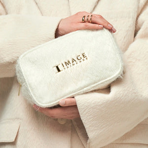 A person wearing a soft beige coat holds a plush white pouch with a gold zipper embossed with the logo "IMAGE Skincare," showcasing the Dazzling Duo | IMAGE Skincare.