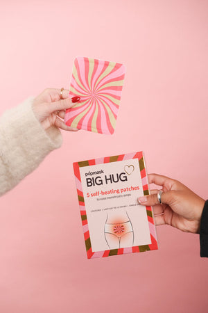 Hands holding a colorful packaging and a pink and red swirled patch for Big Hug - 5 Pack | Popmask self-heating patches designed for menstrual cramp relief on a soft pink background.