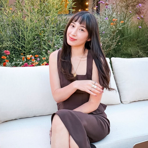 Woman seated on a white outdoor sofa surrounded by flowers, promoting Astrology Lounge (Full Day)- Astrology Readings | Alexa Michaelis
