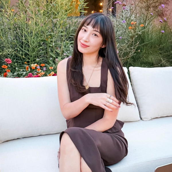 Woman seated on a white outdoor sofa surrounded by flowers, promoting Astrology Lounge (Full Day)- Astrology Readings | Alexa Michaelis