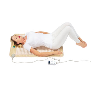 Woman relaxing on a beige wellness mat with controller, demonstrating use of the SOFT Mat Medium 4024 InfraMat Pro® | HealthyLine for body care and recovery.
