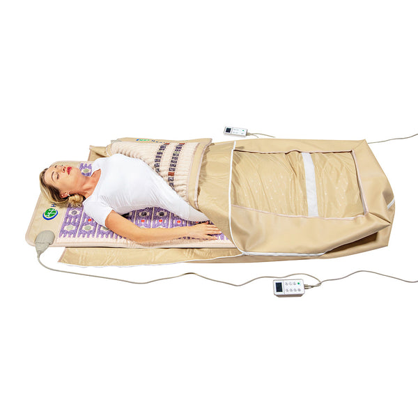 Woman lying relaxed on a wellness device with a beige therapeutic mat and blanket, using the TAJ-Mat™ Full 7224 Firm - Photon PEMF InfraMat Pro® | HealthyLine for body care and recovery.