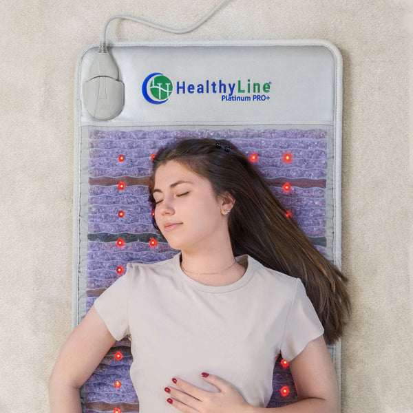 Woman lying peacefully on a wellness device with glowing red lights, demonstrating relaxation and recovery with the Platinum-Mat™ Full Short 6024 Firm - Photon Advanced PEMF InfraMat Pro® | HealthyLine.