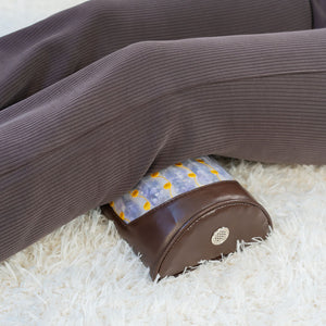 Person using the Amethyst Bolster Firm - Heated InfraMat Pro® | HealthyLine placed under their legs, featuring a brown leather bolster with amethyst and yellow accents, on a white textured surface.
