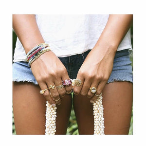 Close-up of a person wearing the Gemstone Fade Bracelet | Catherine Weitzman Jewelry alongside multiple gold rings and holding a shell necklace, dressed in casual summer attire.