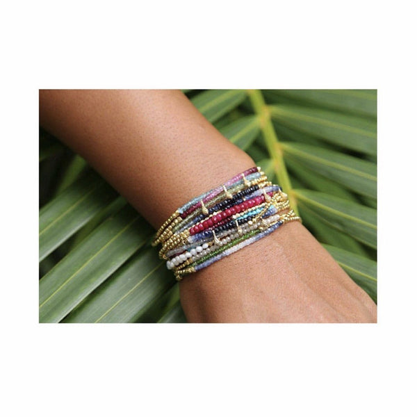Close-up of a wrist wearing the Gemstone Fade Bracelet | Catherine Weitzman Jewelry, featuring colorful beaded strands with gold accents against a green leafy background.
