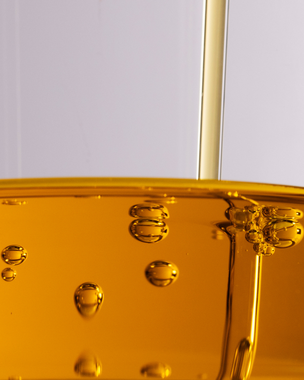 Close-up of golden liquid with bubbles being poured, representing Boost 49% Rosehip Oil Serum | Three Ships, highlighting skincare and wellness benefits.