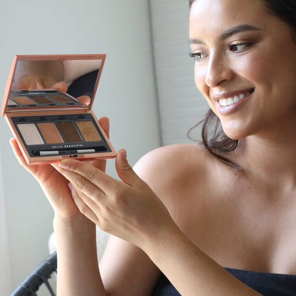 Woman smiling and holding an open La Vie Neutral Eyeshadow Palette | Chella showing neutral shades with a mirror in a bright, natural light setting.
