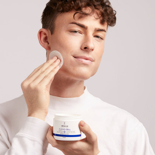 A man gently applies CLEAR CELL salicylic clarifying pads | IMAGE Skincare to his cheek, demonstrating a skincare routine for clearer, healthier skin.