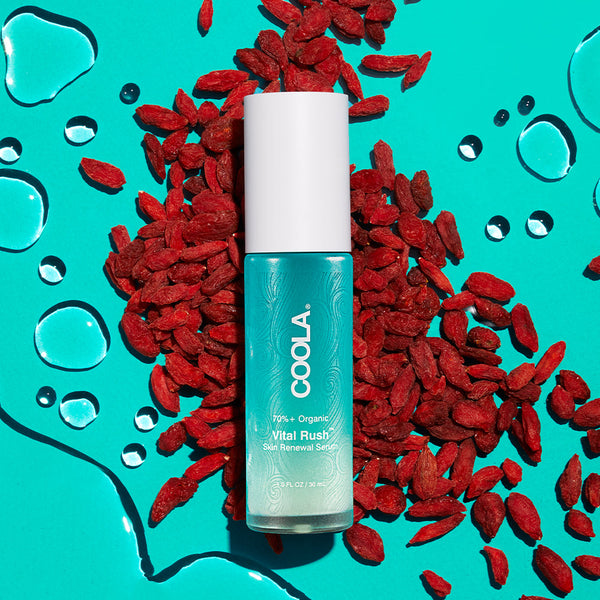 Vital Rush™ Skin Renewal Serum | COOLA bottle on a vibrant turquoise background surrounded by red berries and water droplets, highlighting skincare and natural ingredients.