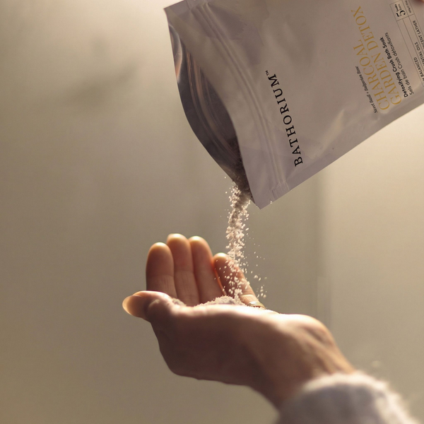 Charcoal Garden Detox Crush | Bathorium pouch pouring powder into an open hand for a body care ritual in warm natural light