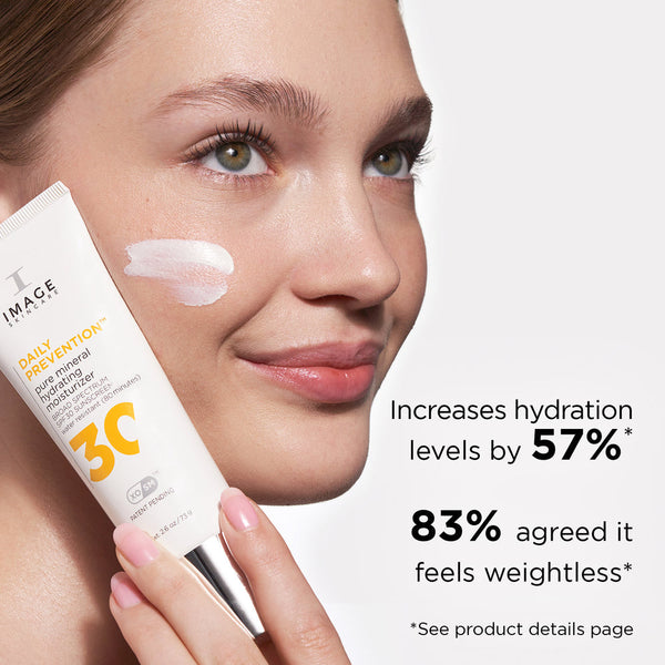 Close-up of a woman applying DAILY PREVENTION Pure Mineral Hydrating Moisturizer SPF 30 | IMAGE Skincare on her cheek, showcasing hydration benefits and lightweight feel claims.