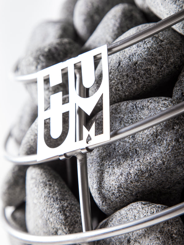 Close-up of smooth sauna stones held in a metal basket with a decorative cutout, part of the E7G Barrel Sauna - 4-6 Person | Western Sol, highlighting quality materials for wellness and relaxation.